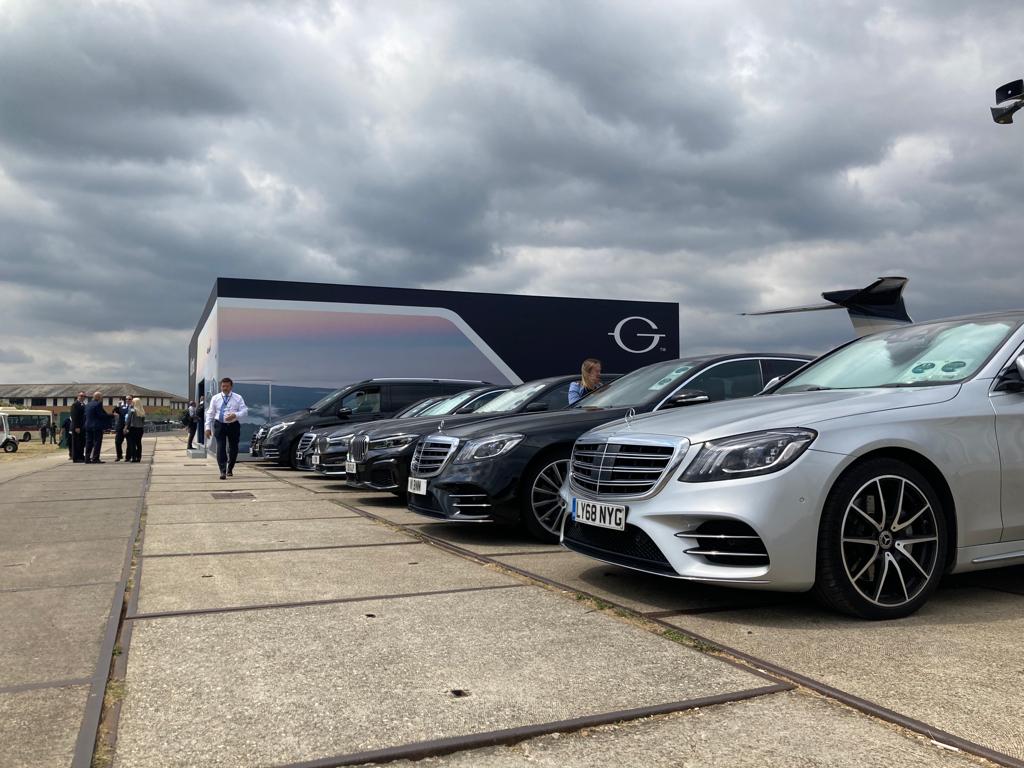 fleet-of-luxury-vehicles-lined-up-at-airshow-with-aircraft-in-background