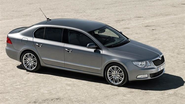 Grey Skoda Superb parked on pale sand, seen from the front three-quarter angle