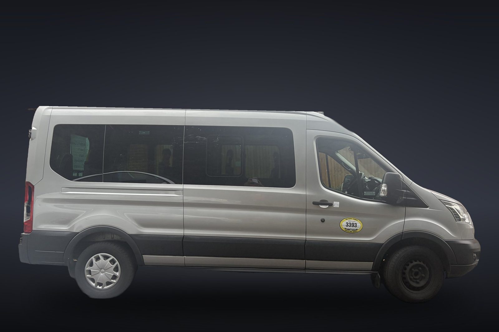 Silver minibus in side view, with a Wiltshire Council private hire plate on the front door