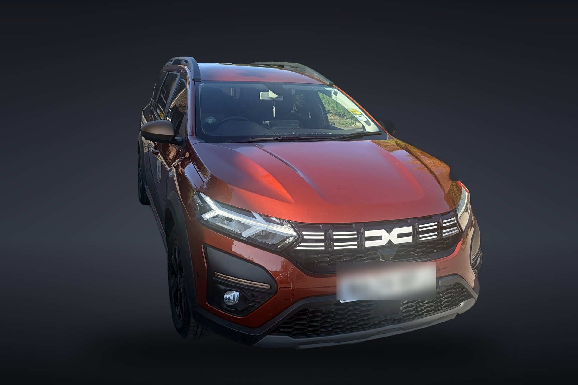 Orange Dacia Jogger seen from the front, on a dark charcoal background